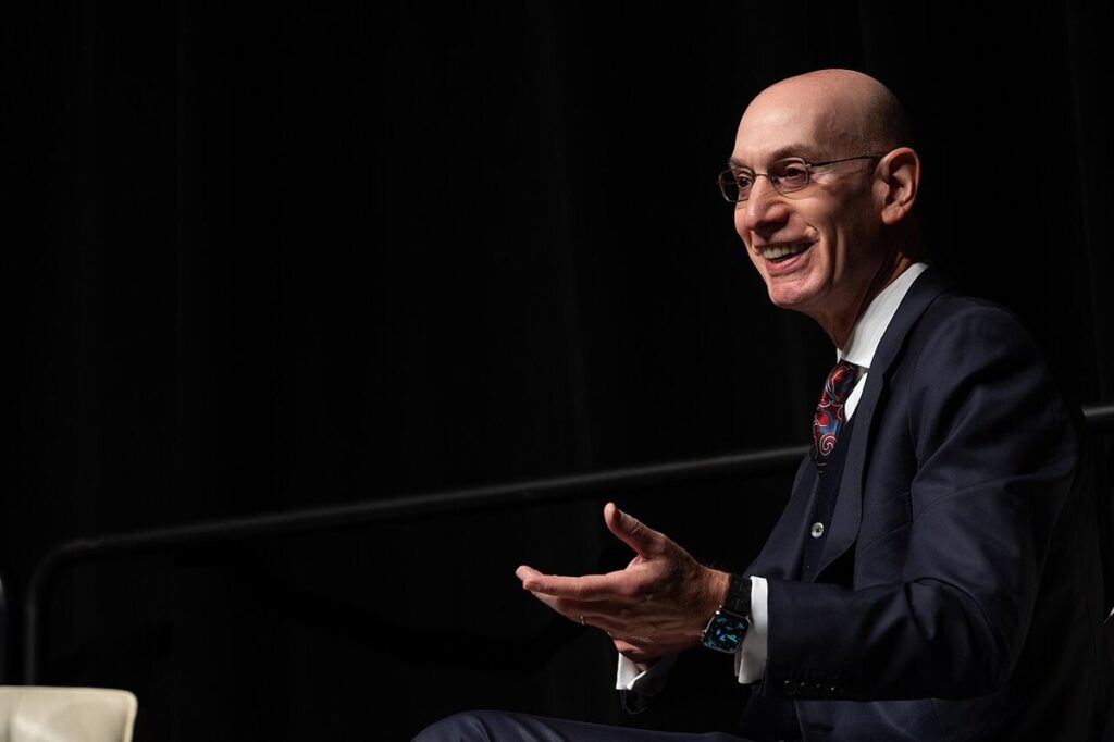 NBA commissioner Adam Silver smiling and gesturing while speaking on stage