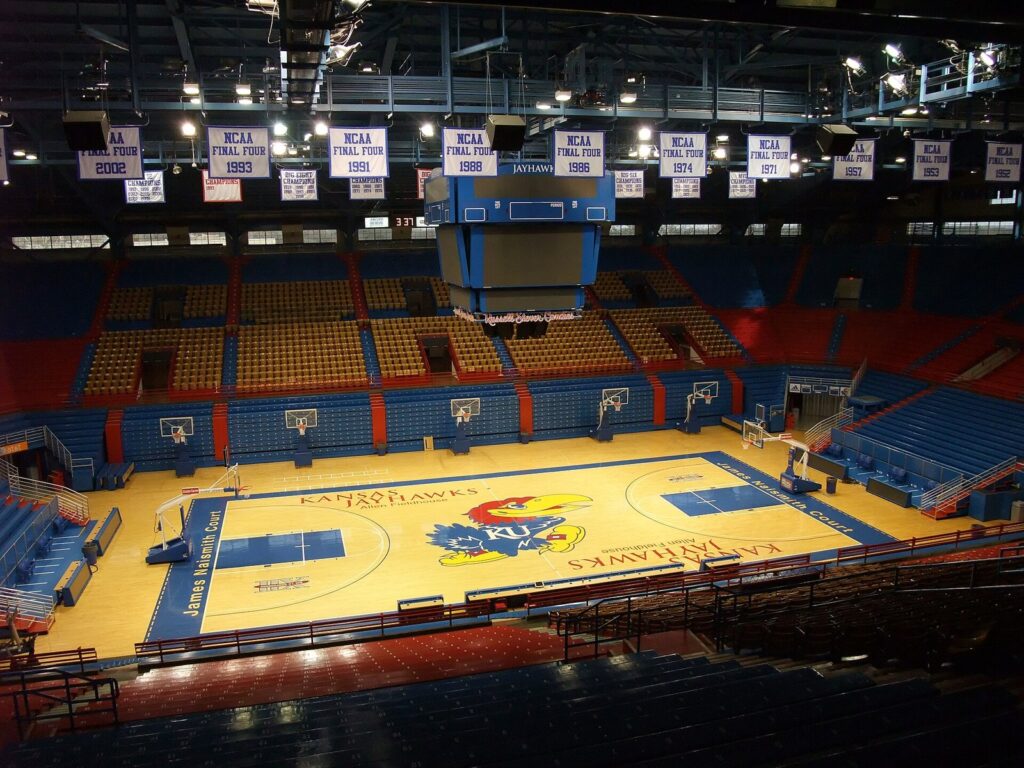 Interior of Allen Fieldhouse in Lawrence, Kansas, with the Jayhawks logo at center court and Final Four banners overhead