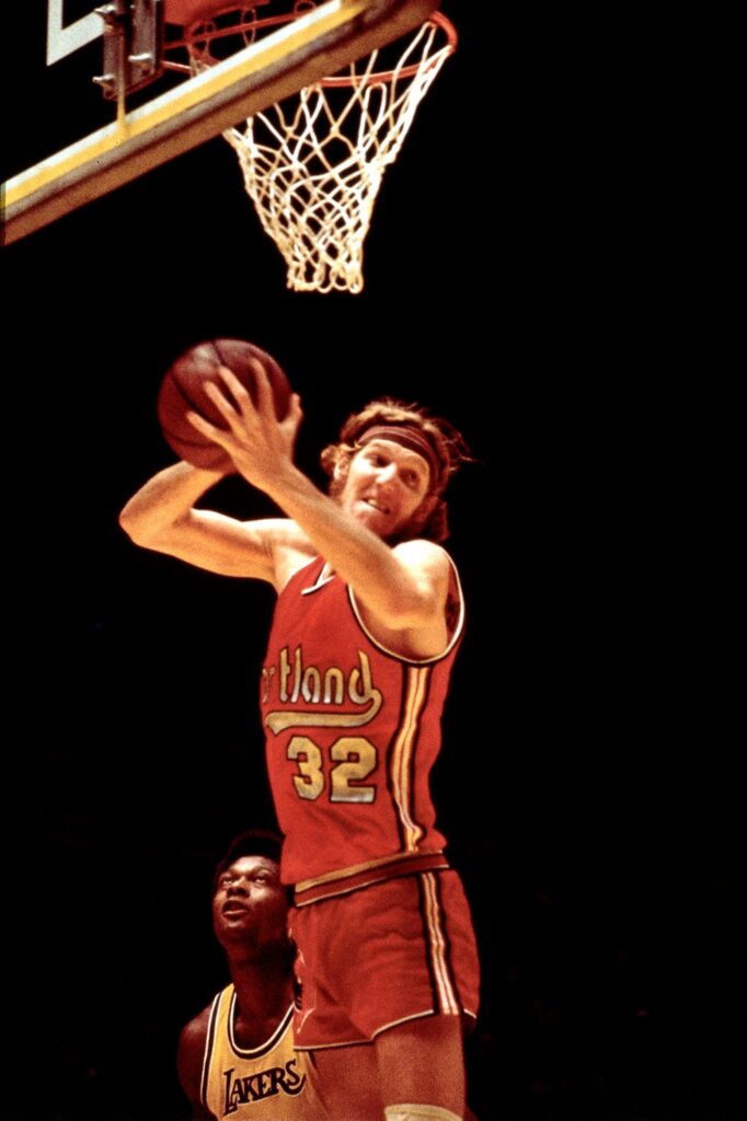 Bill Walton in a red Portland jersey, number 32, rising for a shot near the rim in 1975