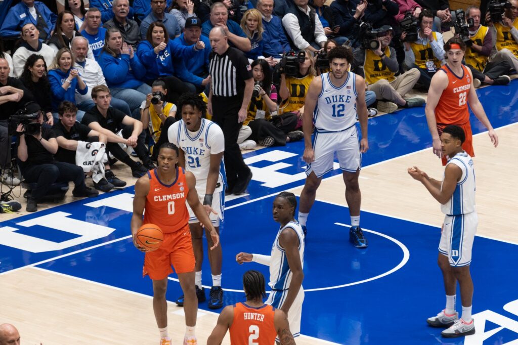 Cameron Boozer, wearing No. 12 for Duke, stands near the free-throw lane with Duke teammates and Clemson players during a game at Cameron Indoor Stadium