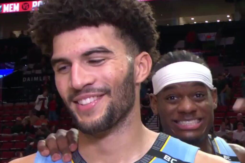 Cameron Boozer of the Memphis Grizzlies smiles as a teammate leans in during his postgame interview after his triple-double in Portland