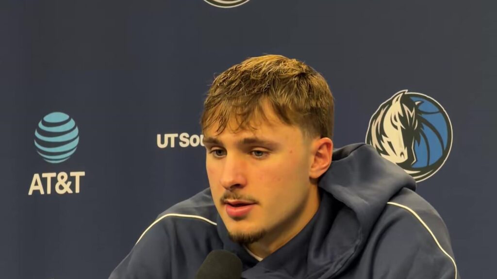 Cooper Flagg in a navy hoodie speaking at a Mavericks postgame news conference