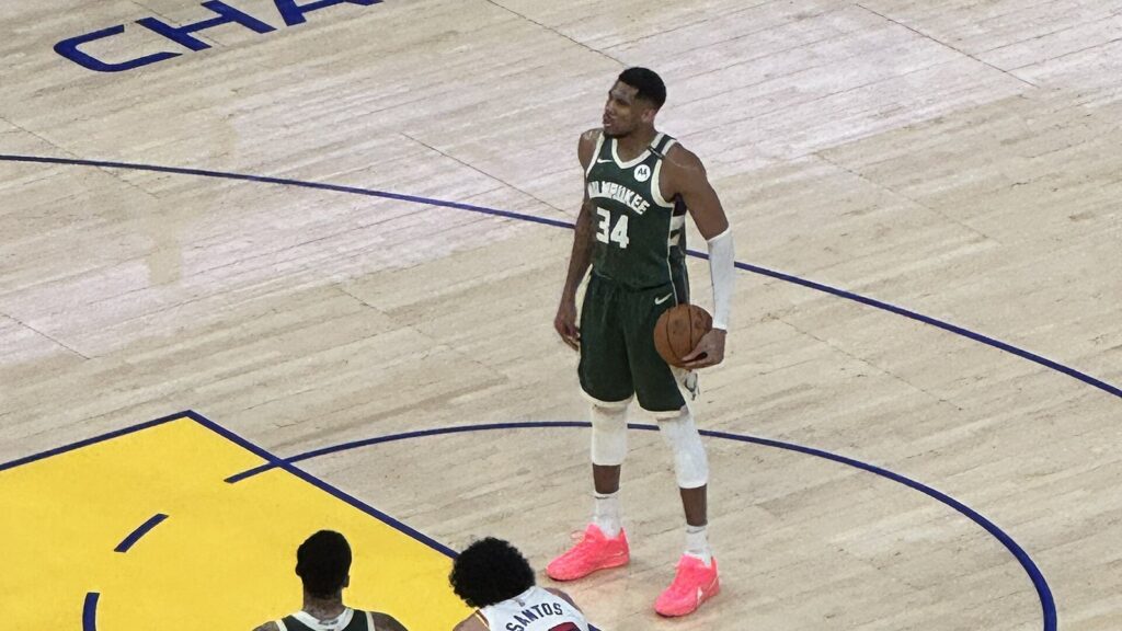 Giannis Antetokounmpo in a green Bucks uniform at the free-throw line against the Warriors, with Draymond Green and two other players lined up on the lane