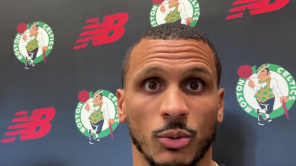 Celtics coach Joe Mazzulla speaks to reporters at shootaround in front of a Celtics backdrop