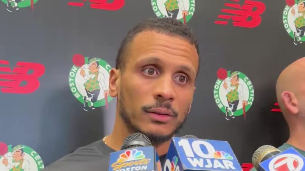 Boston Celtics coach Joe Mazzulla speaking to reporters in front of a Celtics backdrop after practice