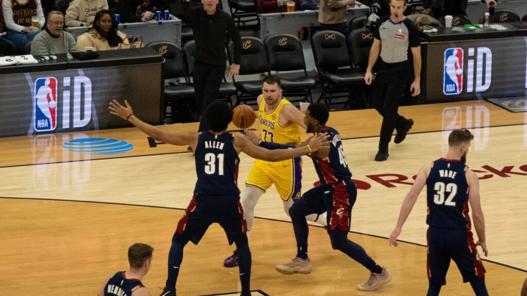Luka Dončić of the Los Angeles Lakers holding the ball as Jarrett Allen and Donovan Mitchell of the Cleveland Cavaliers defend him
