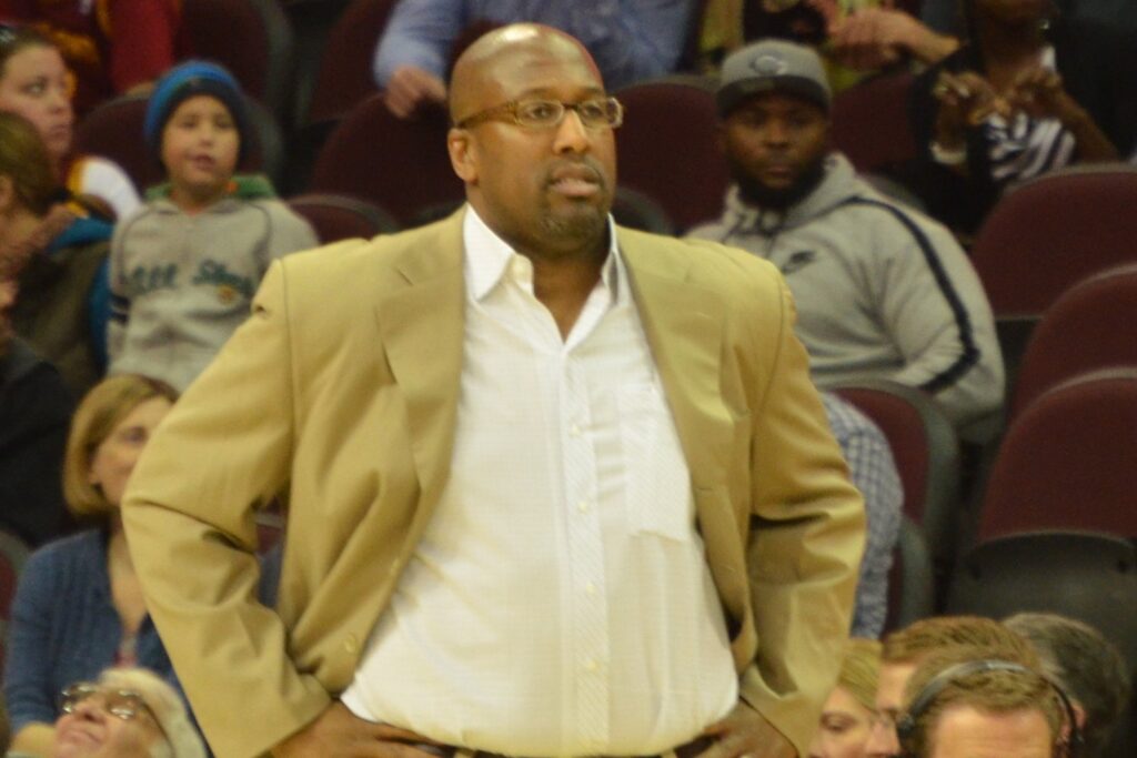 Mike Brown stands on the sideline with his hands on his hips in a tan suit