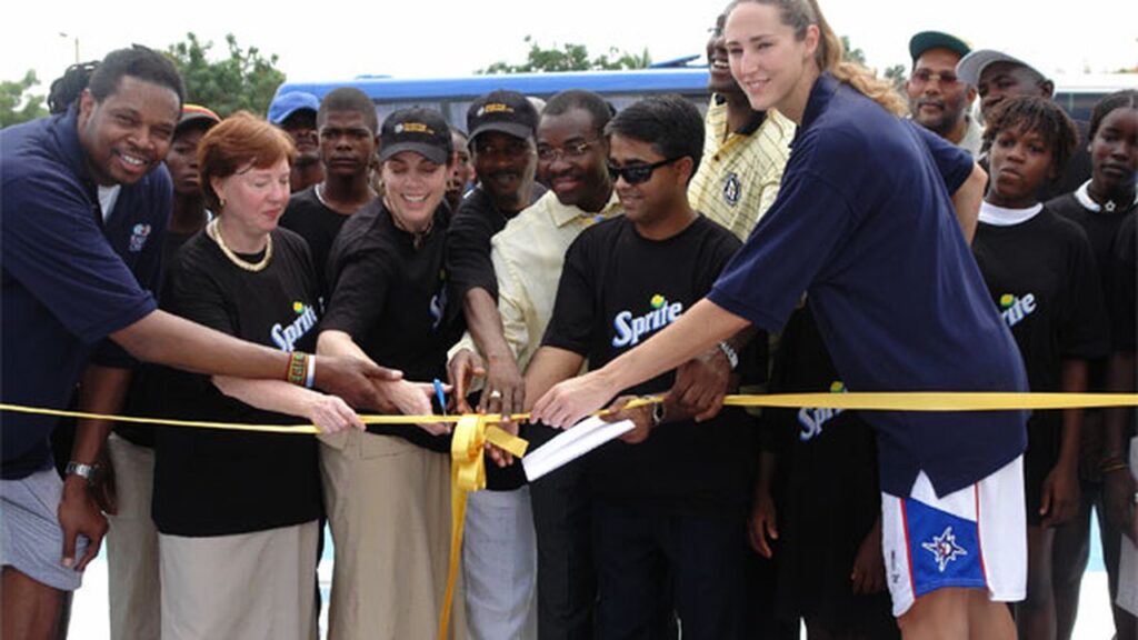 NBA legend Sam Perkins, U.S. officials and a young participant cut a ribbon at a basketball court dedication in Angola