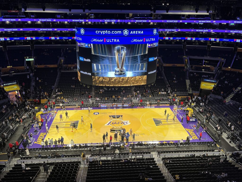 Wide view of a brightly colored purple and gold NBA Cup court inside the Lakers' arena with the Cup trophy on the video board