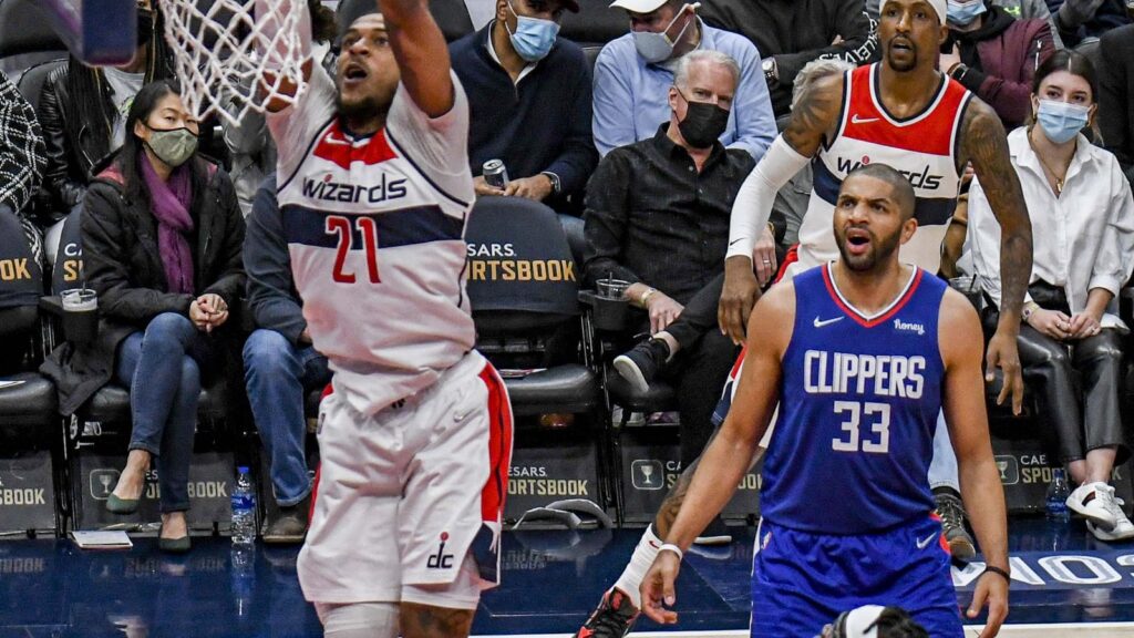 Nicolas Batum in a blue LA Clippers No. 33 jersey on the court in Washington as a Wizards player goes up for a dunk