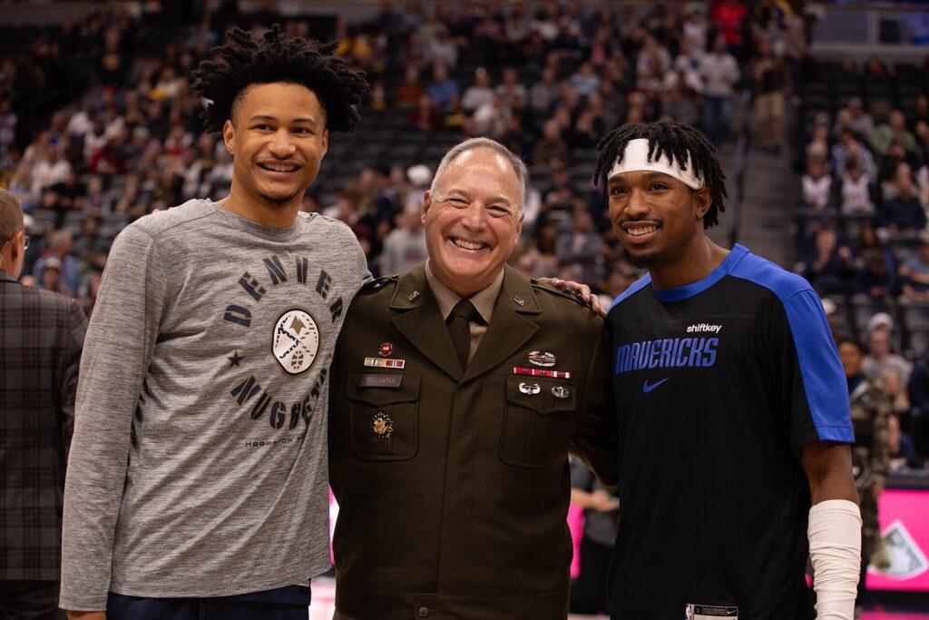 Trey Alexander of the Nuggets and Brandon Williams of the Mavericks pose with an Army Reserve general on the Ball Arena court