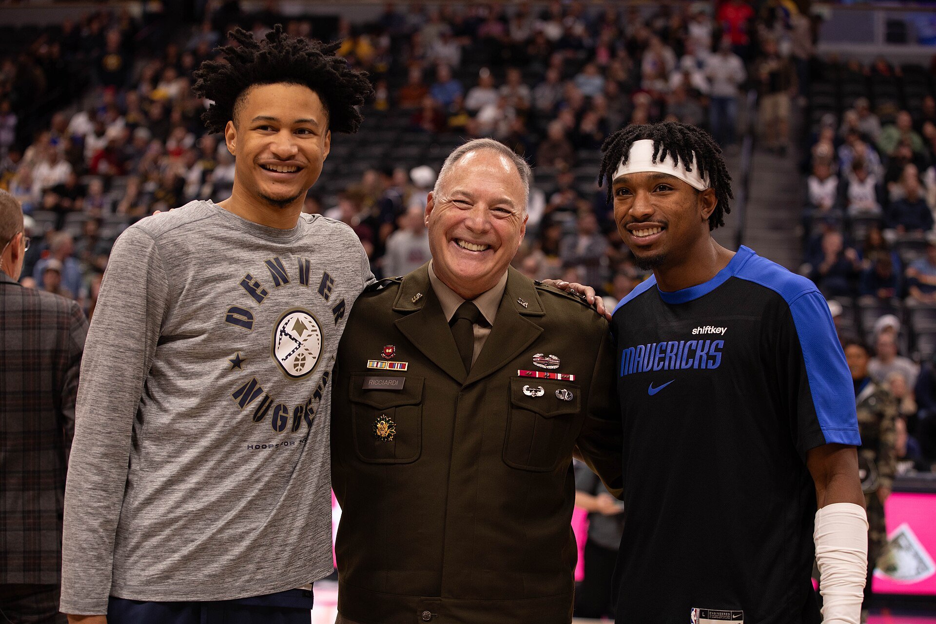 Trey Alexander of the Nuggets and Brandon Williams of the Mavericks pose with an Army Reserve general on the Ball Arena court